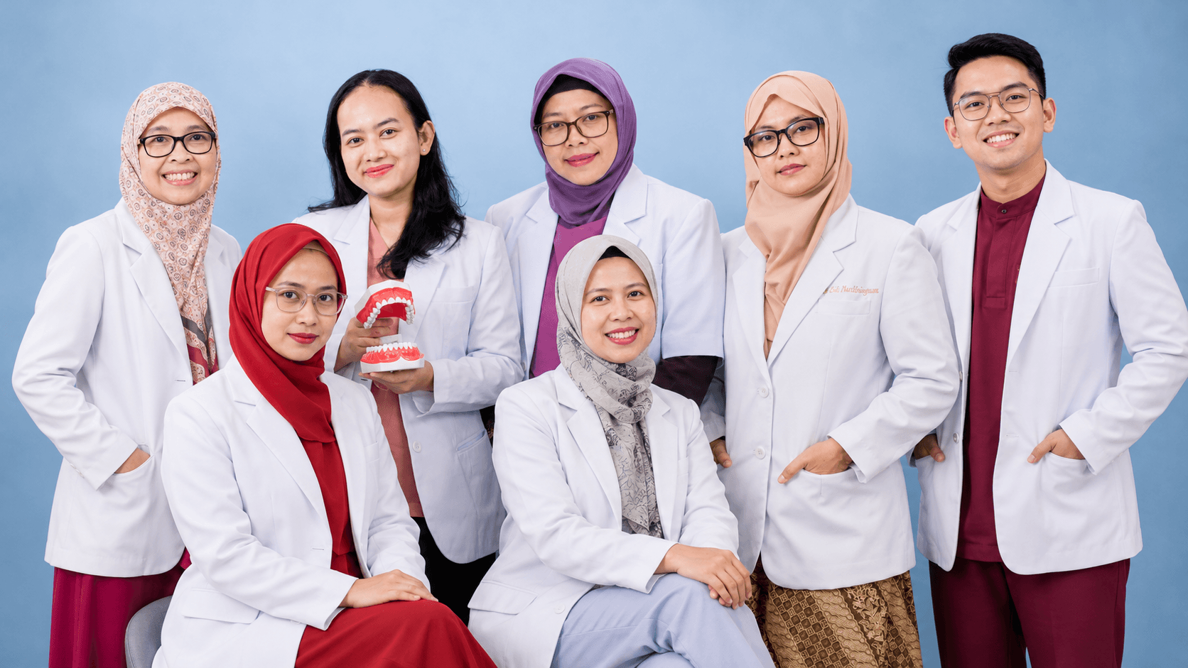 Tim dokter Sanafa Dental Clinic berfoto bersama dengan jas putih di studio berlatar biru muda
